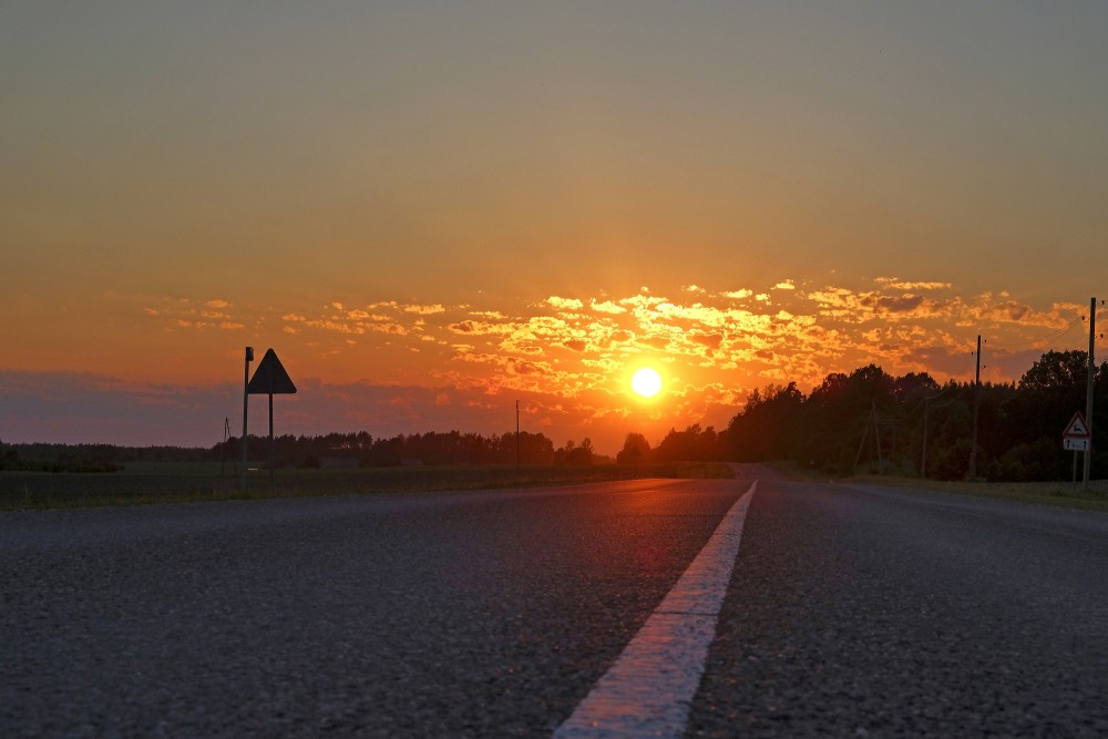 Krāšņa saulrieta ainava, saule atspīd uz asfaltēta ceļa Krāšņa saulrieta ainava, saule atspīd uz asfaltēta ceļa
