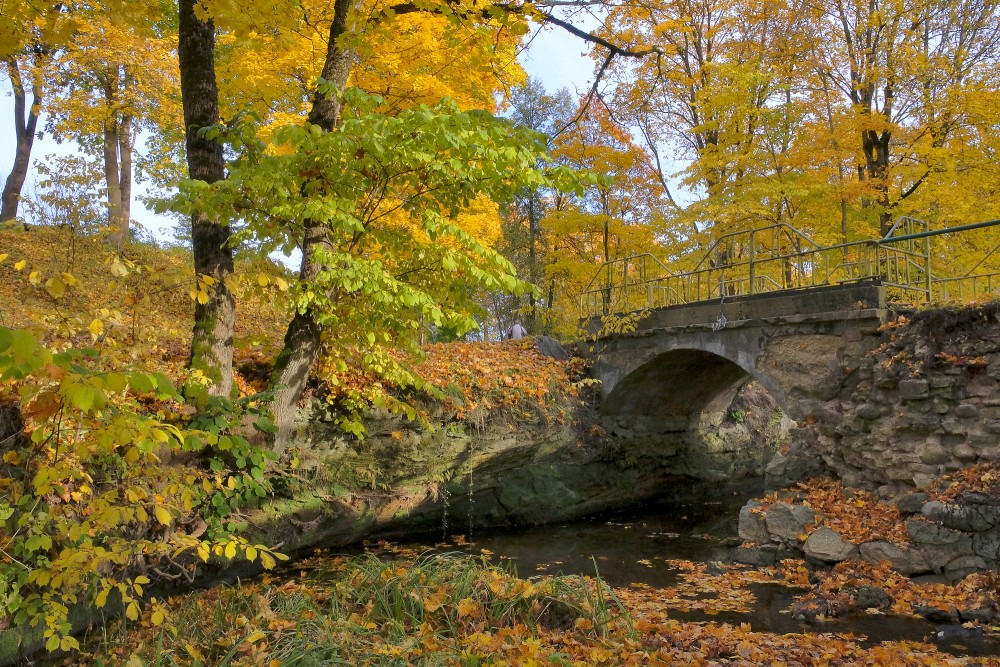Historic stone bridge with metal railings in a golden autumn park