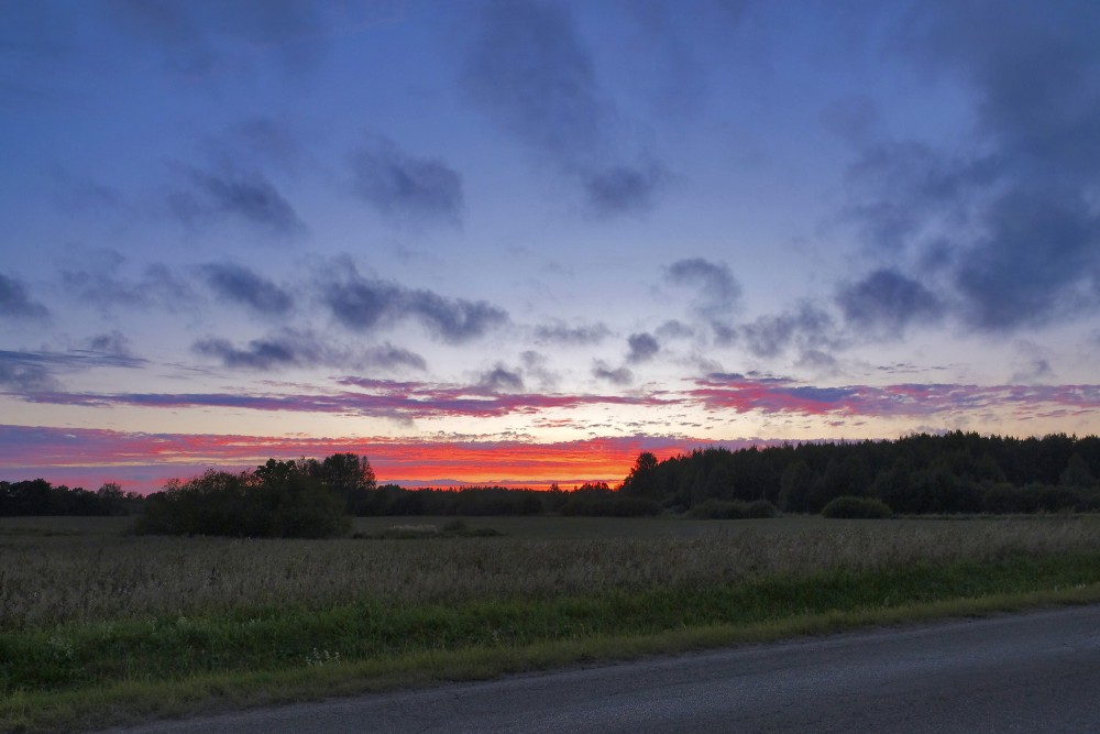 Red sunset over a meadow and forest line with dramatic cloud bands