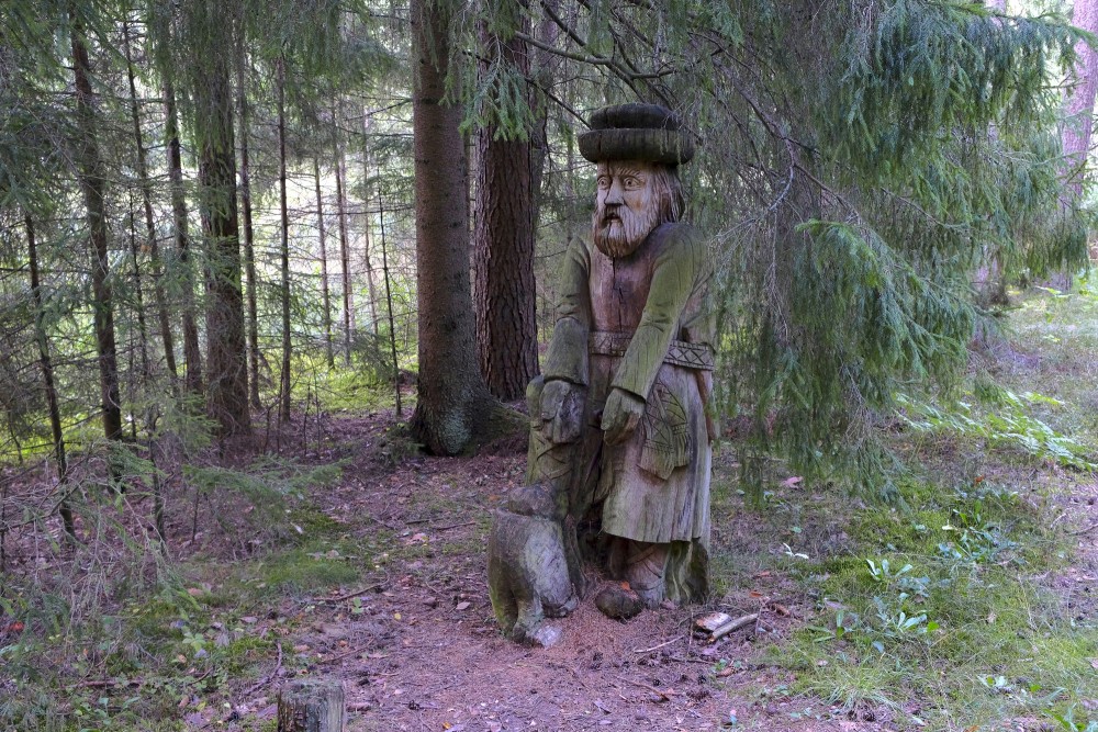Wooden sculpture in the forest with a seated figure and an animal carving
