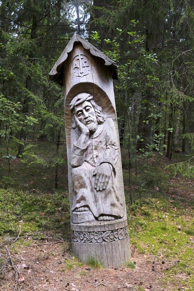 Wooden relief sculpture of a man under a small roof by a forest trail
