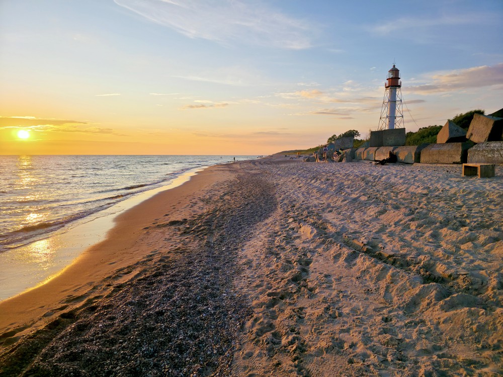 White lighthouse and concrete blocks on a sandy beach at sunset