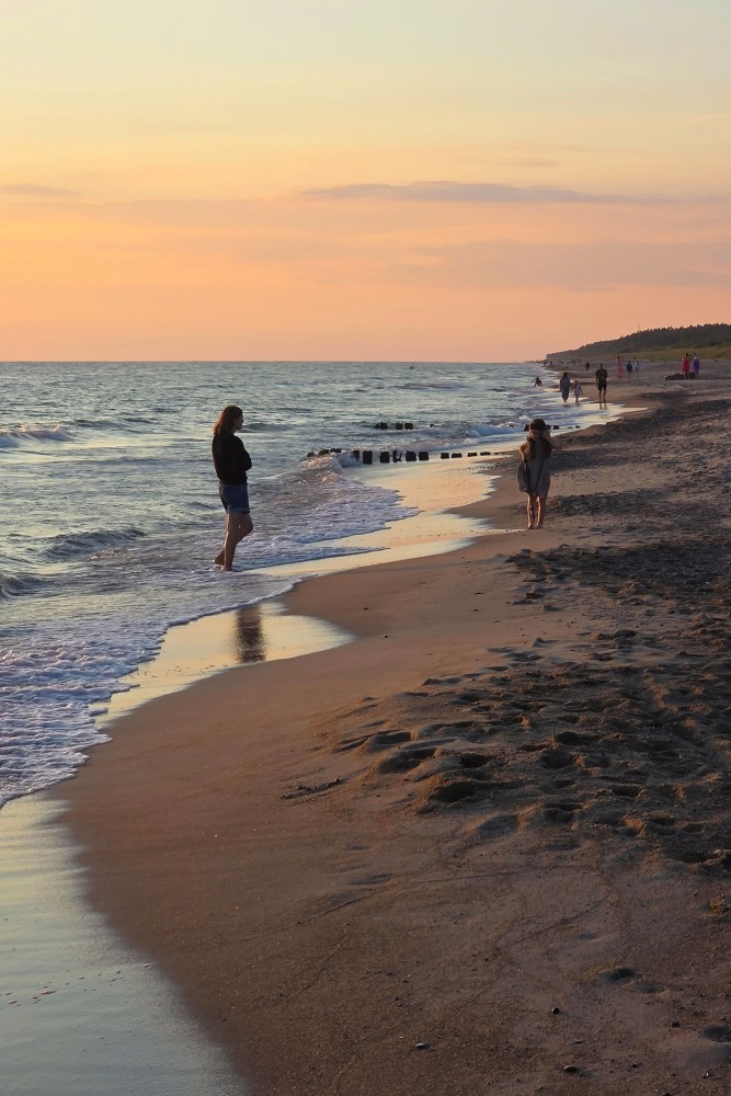 Evening walk on the beach during sunset with wooden pier in the sea