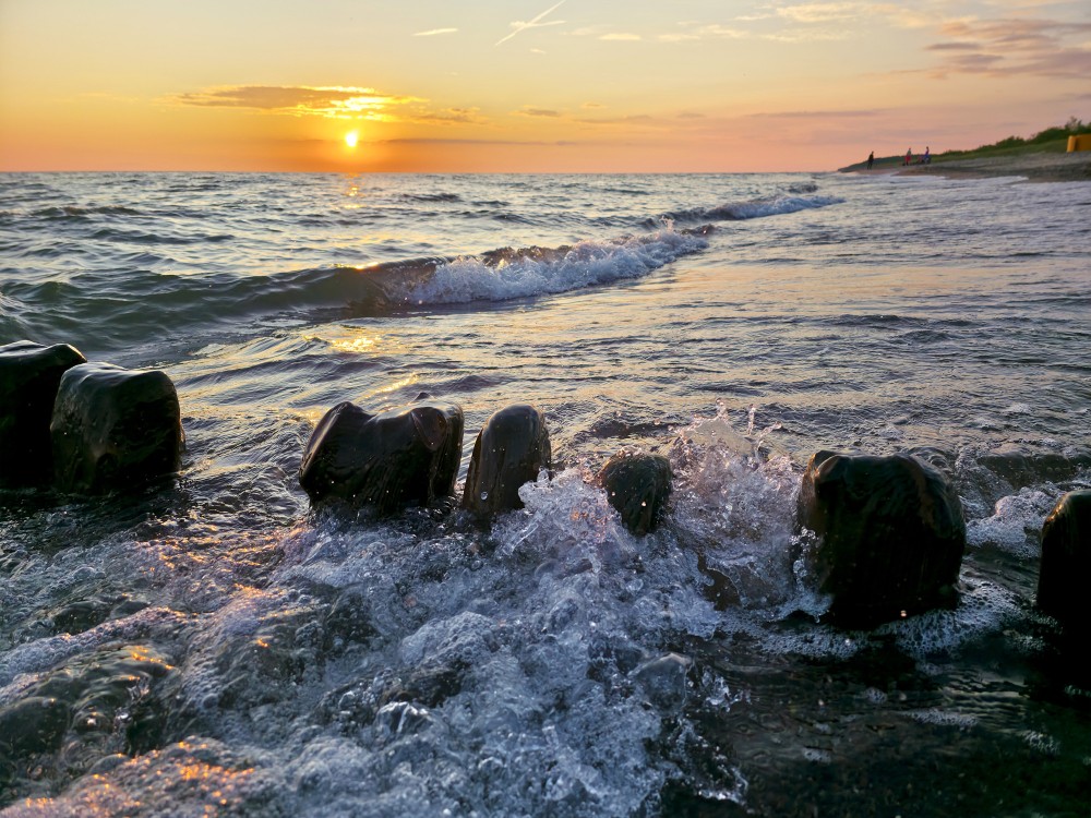 Sunset sea with waves around old, dark wooden pier on the shoreline