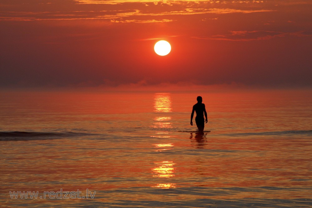 Cilvēka siluets jūrā, saulrietā