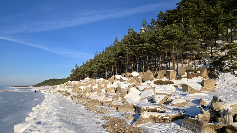Concrete coastal reinforcements and Užava lighthouse in winter landscape