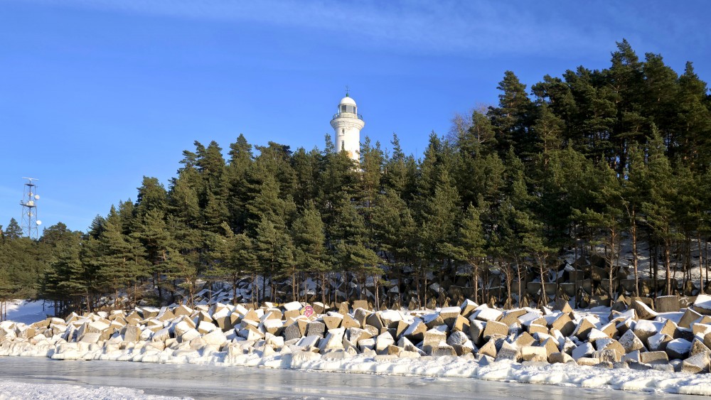 View of the white Užava lighthouse from the frozen seashore