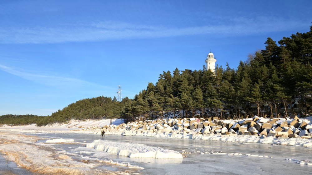 Winter landscape at Užava beach with lighthouse and walkers on ice