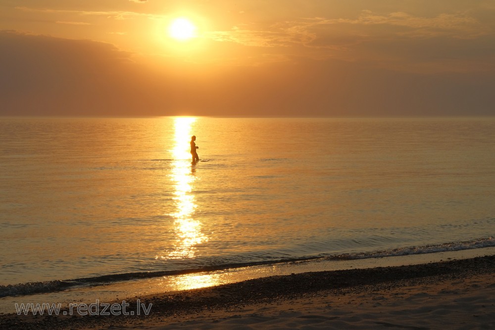Sievietes siluets saulrietā, jūrā