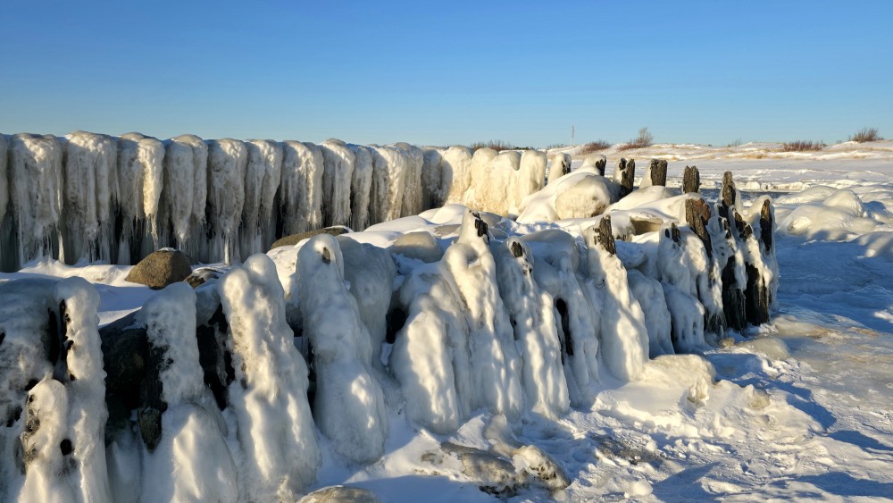 Snowy wooden piles of Pape canal in bright winter sun