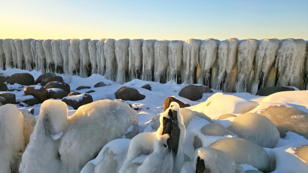 Icy coastal rocks and wooden piles in the Pape canal