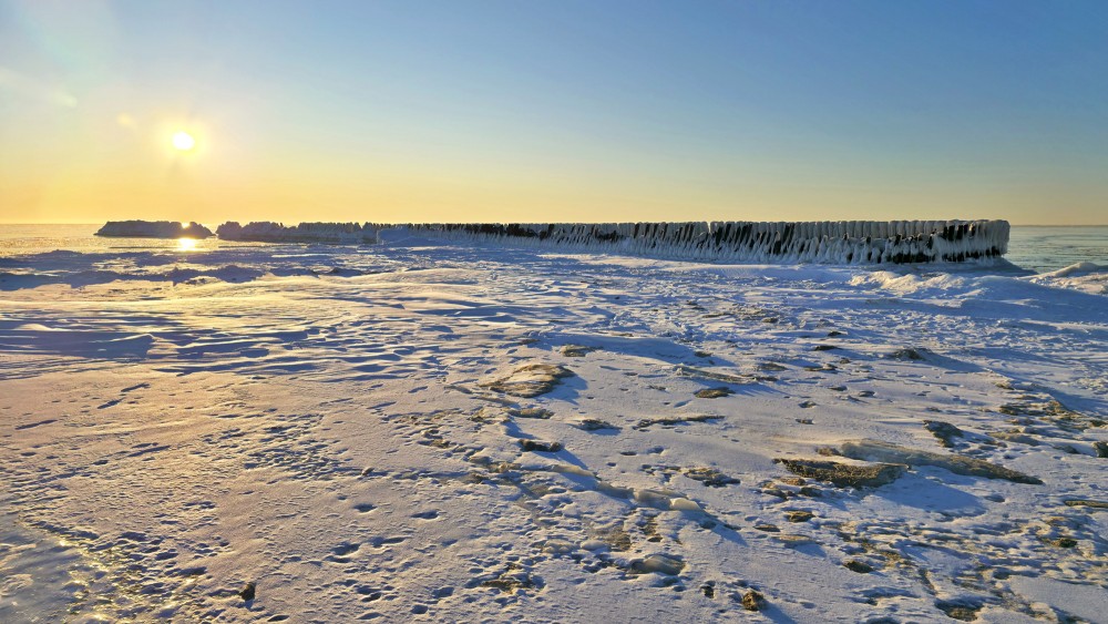 Sunset over the icy Pape wooden groynes in winter