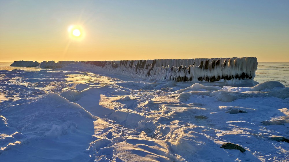 Winter sun glowing over icy wooden groynes in Pape