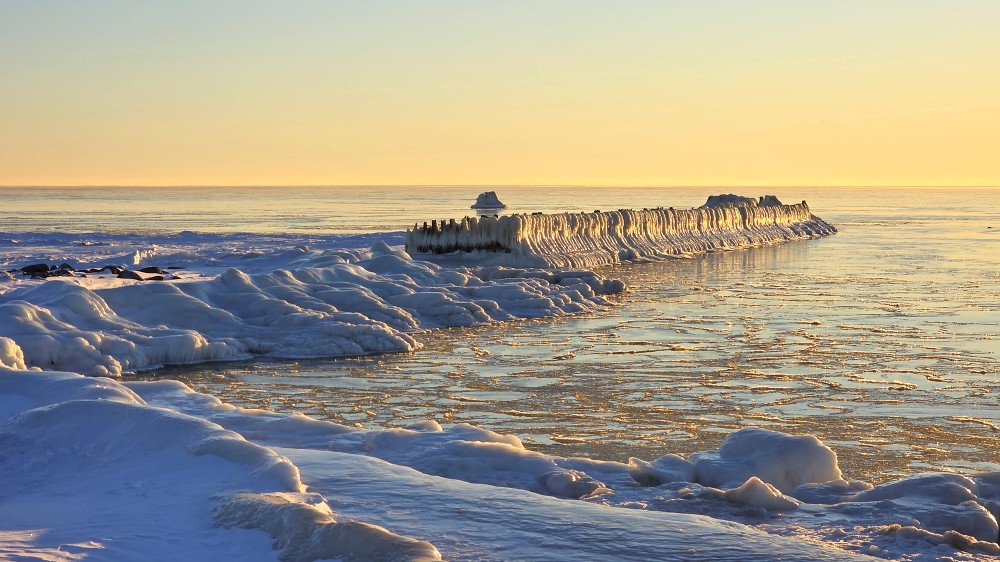 Icy Pape wooden groynes and frozen sea at sunset