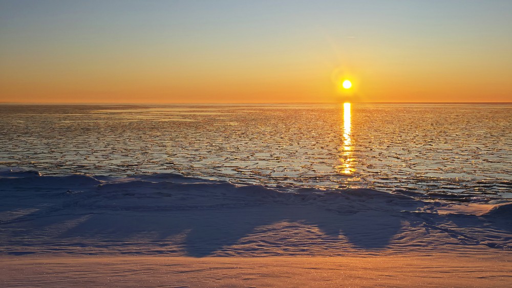 Sunset over a frozen sea landscape with a snowy shore