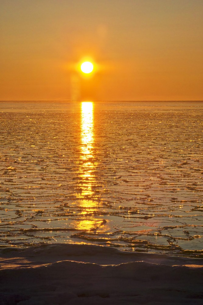 Vertical sunset landscape with a golden light path on ice