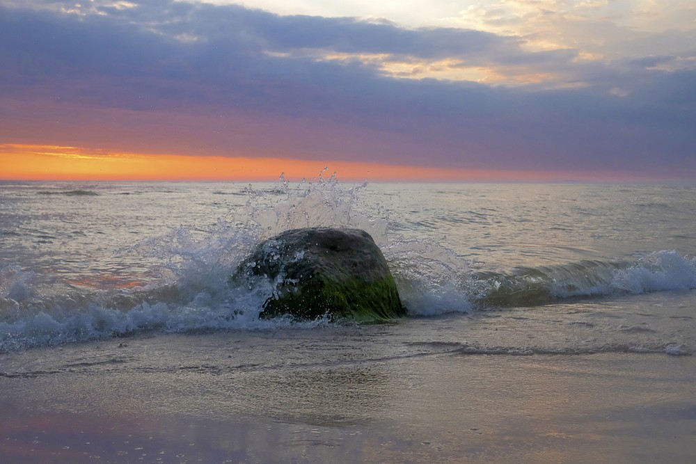 Jūra, akmens un viļņu šļakatas saulrietā