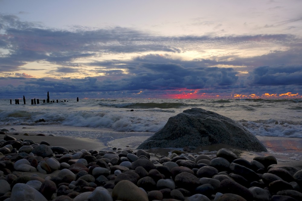 Saulrieta ainava ar akmeni pludmalē