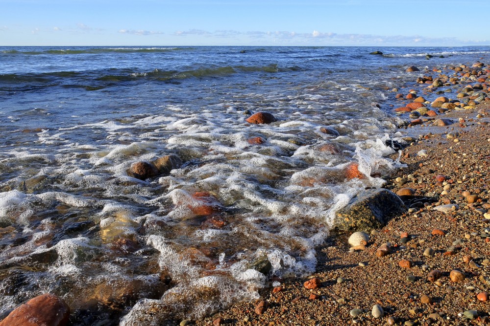 Wide beach landscape with waves and colorful pebbles at sunset