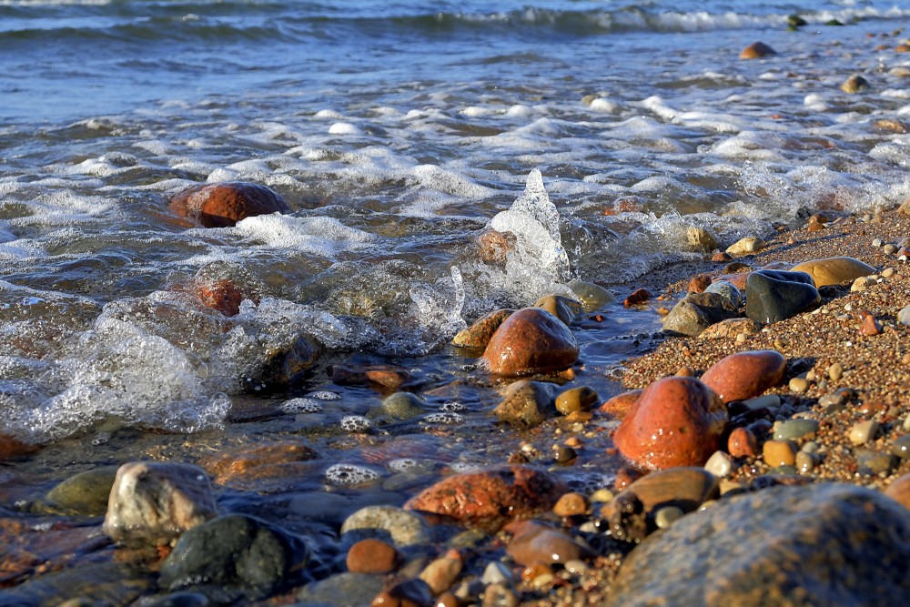 Waves splashing over orange and red pebbles on a sunny beach