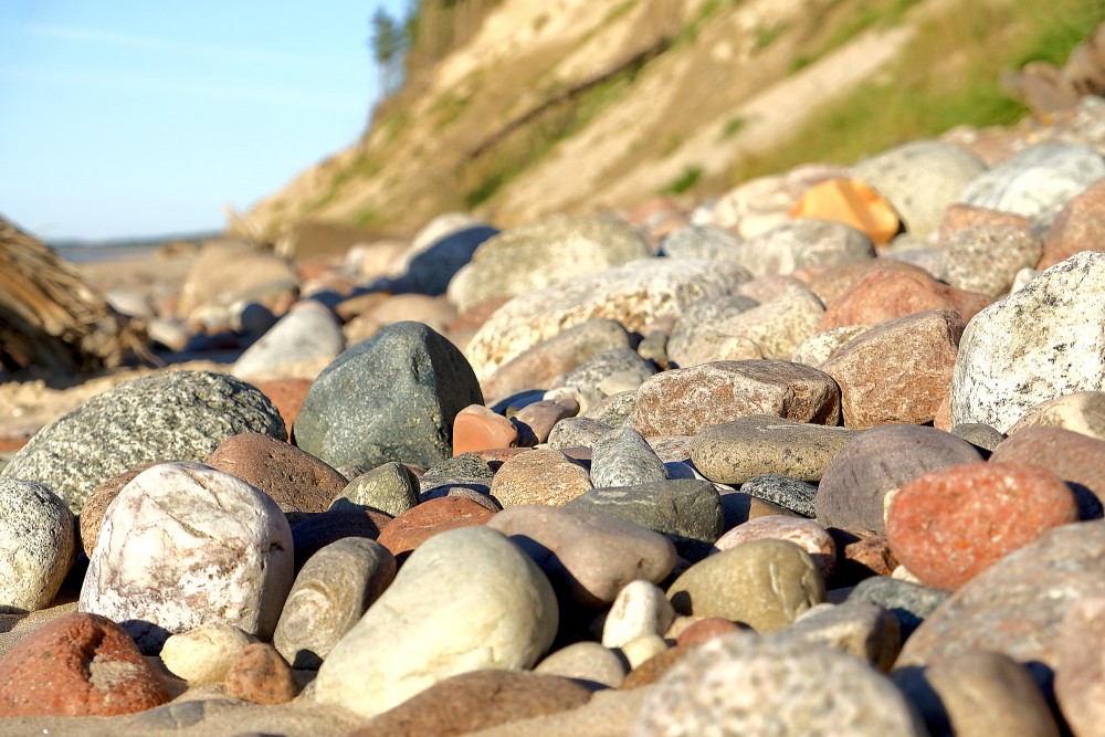 Large pebbles on a sandy beach with a steep bank in the background