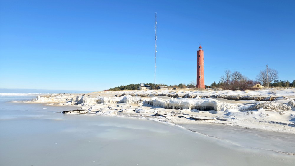 Frozen coast and Akmensrags Lighthouse on a sunny winter day
