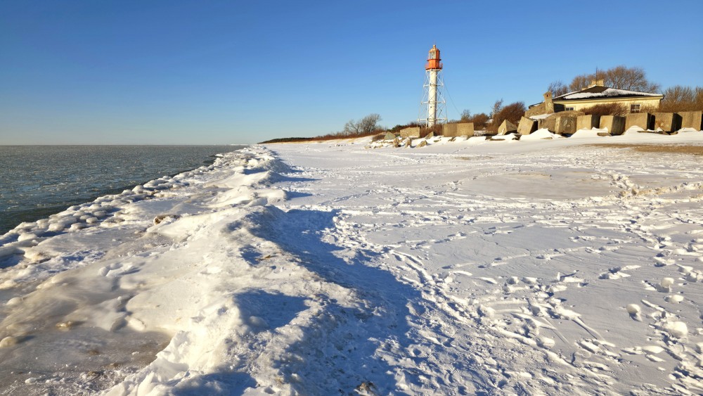 Pape lighthouse behind an icy beach and snow ridges