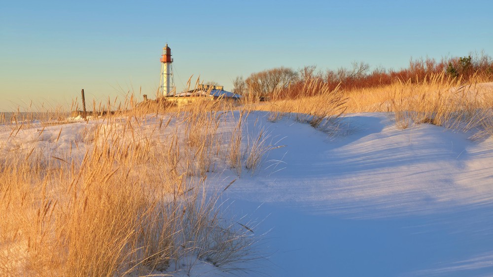 Pape lighthouse behind snowy dunes and golden grass